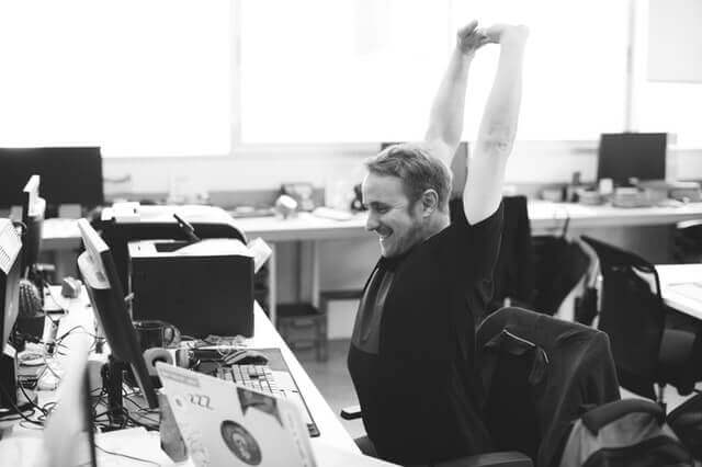 black and white image of man stretching at his desk